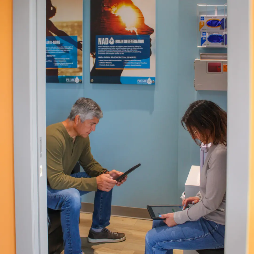 Two clients seated in the intake room at Prime IV Hydration & Wellness in Huntsville, AL, completing their check-in forms on tablets